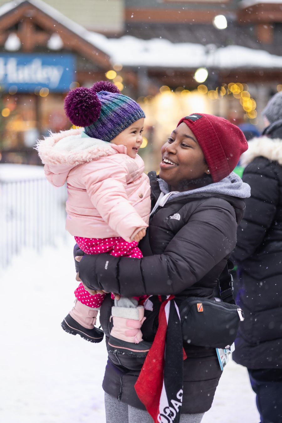 Mom holding her baby, both smiling wide and enjoying Winter in the Village.