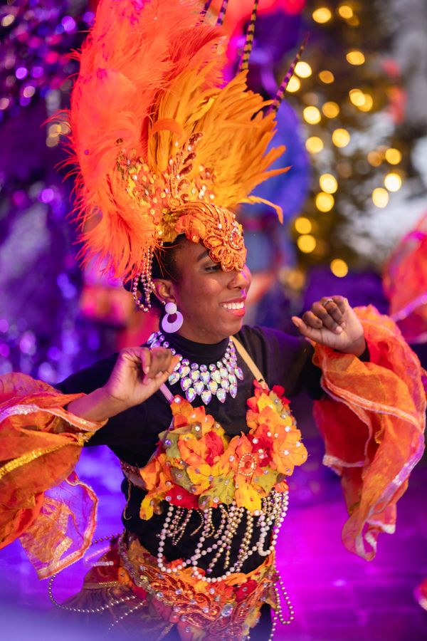 Closeup shot of Caribbean Winterfest performer, adorned in orange feathers and jewels, dancing on the Subaru Stage.