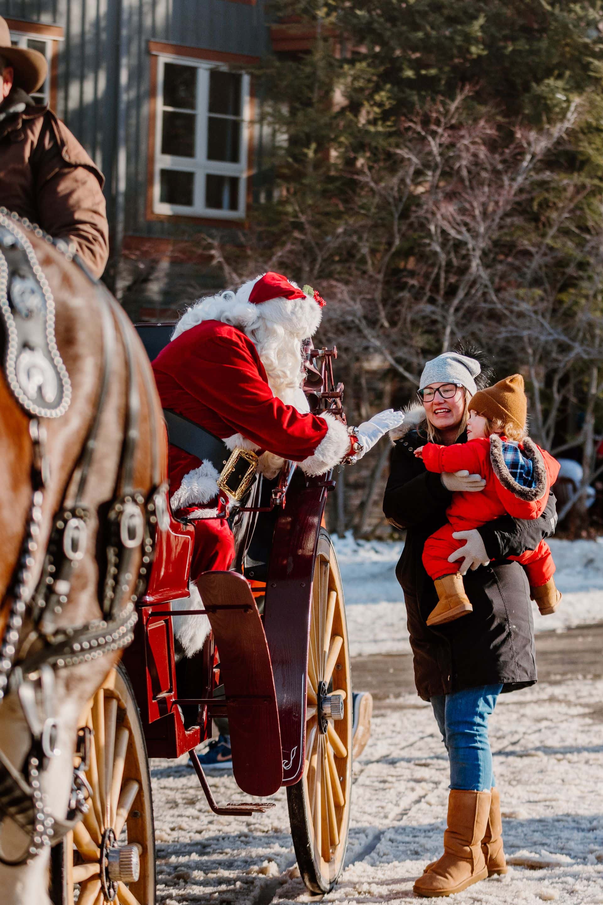 Mom holding her toddler up to see Santa on his horse & carriage during Holiday Magic in the Village.