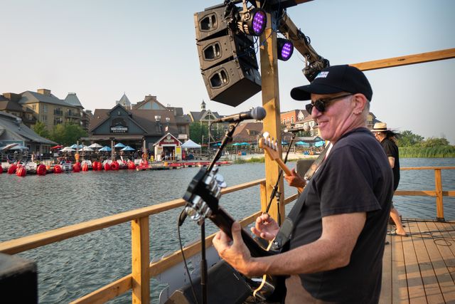 Live band rocking out of the Floating Stage with views of the Village patios on a warm evening at sunset.